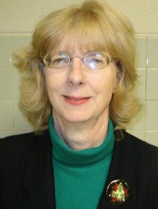 Woman with glasses wearing green turtleneck and brooch